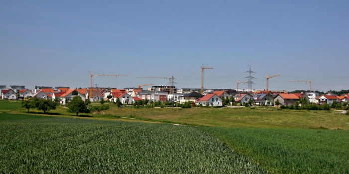 Neubaugebiet am Ortsrand mit Einfamilienhäusern und Kränen; davor Felder – Beispiel für wachsenden Flächenverbrauch
